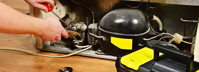 Refrigerator repair technician fixing the compressor and wiring in Pearl, MS
