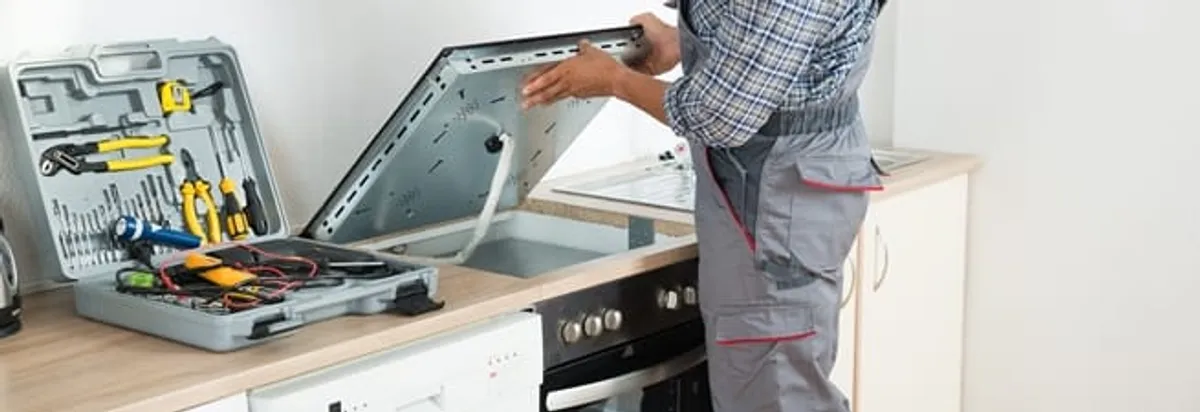 Cooktop repair technician lifting a built-in stovetop for service in Jackson, MS