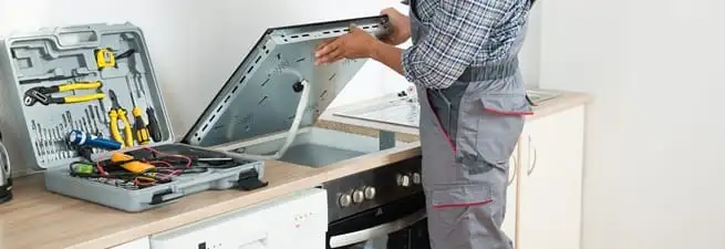 Cooktop repair technician lifting a built-in stovetop for service in Jackson, MS