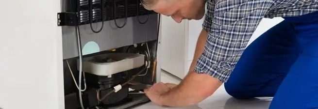Refrigerator repair technician servicing the compressor and condenser area in Jackson, MS
