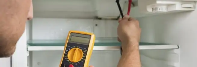 Refrigerator repair technician testing electrical components with a multimeter in Jackson, MS
